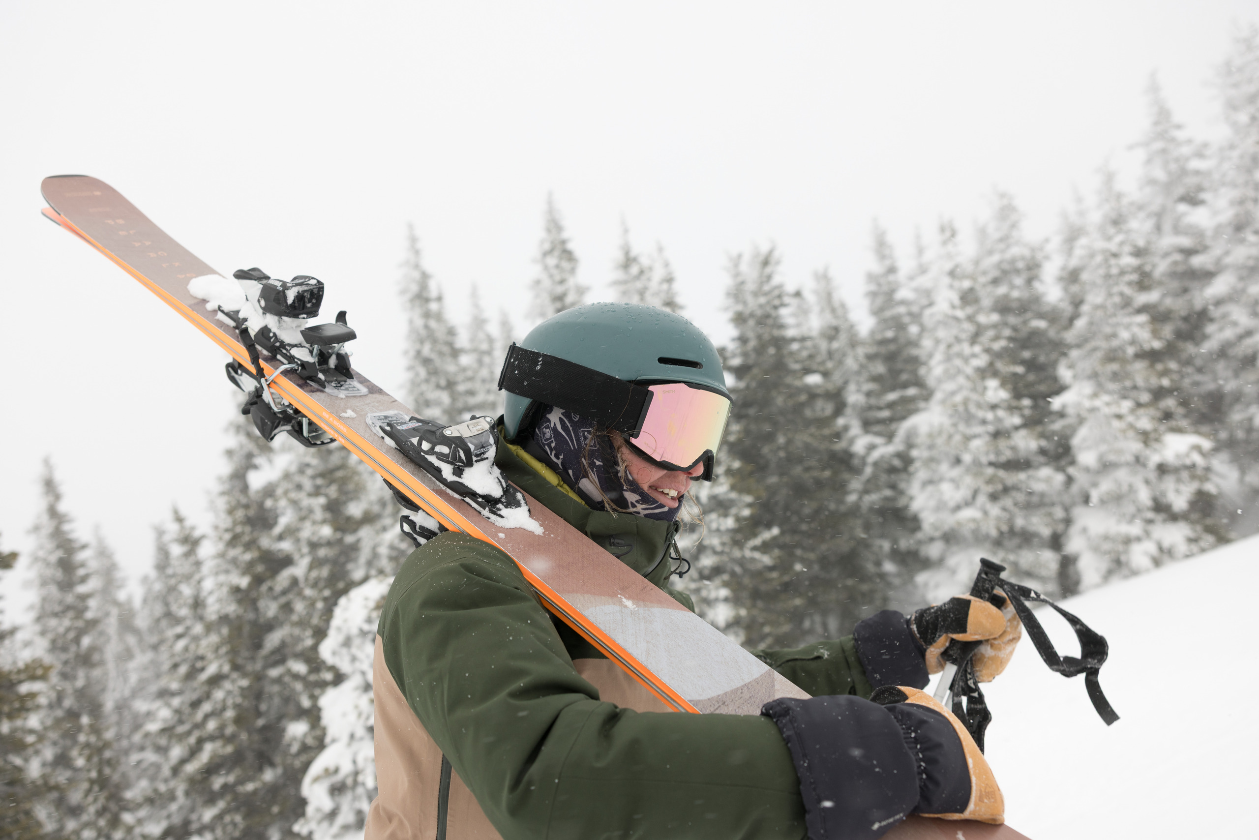A skier wearing a helmet and goglges carries skis on her shoulder