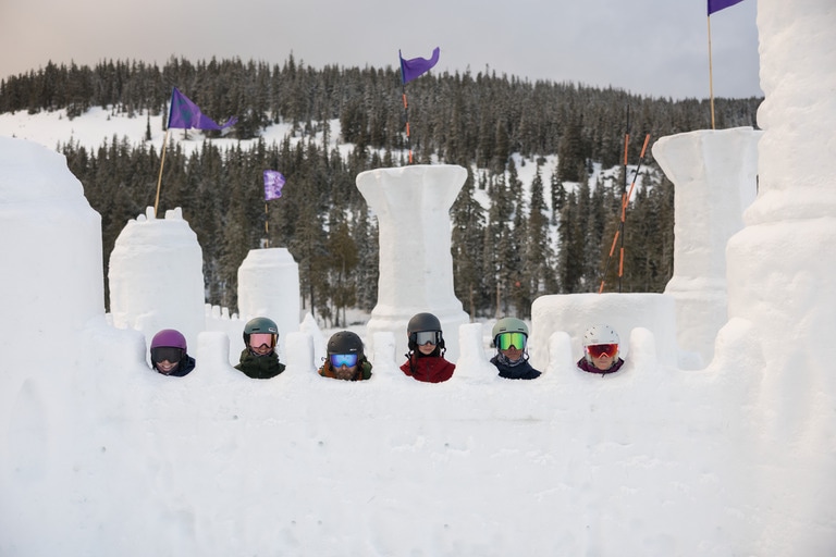 Six people wearing helmets and goggles at a snow castle