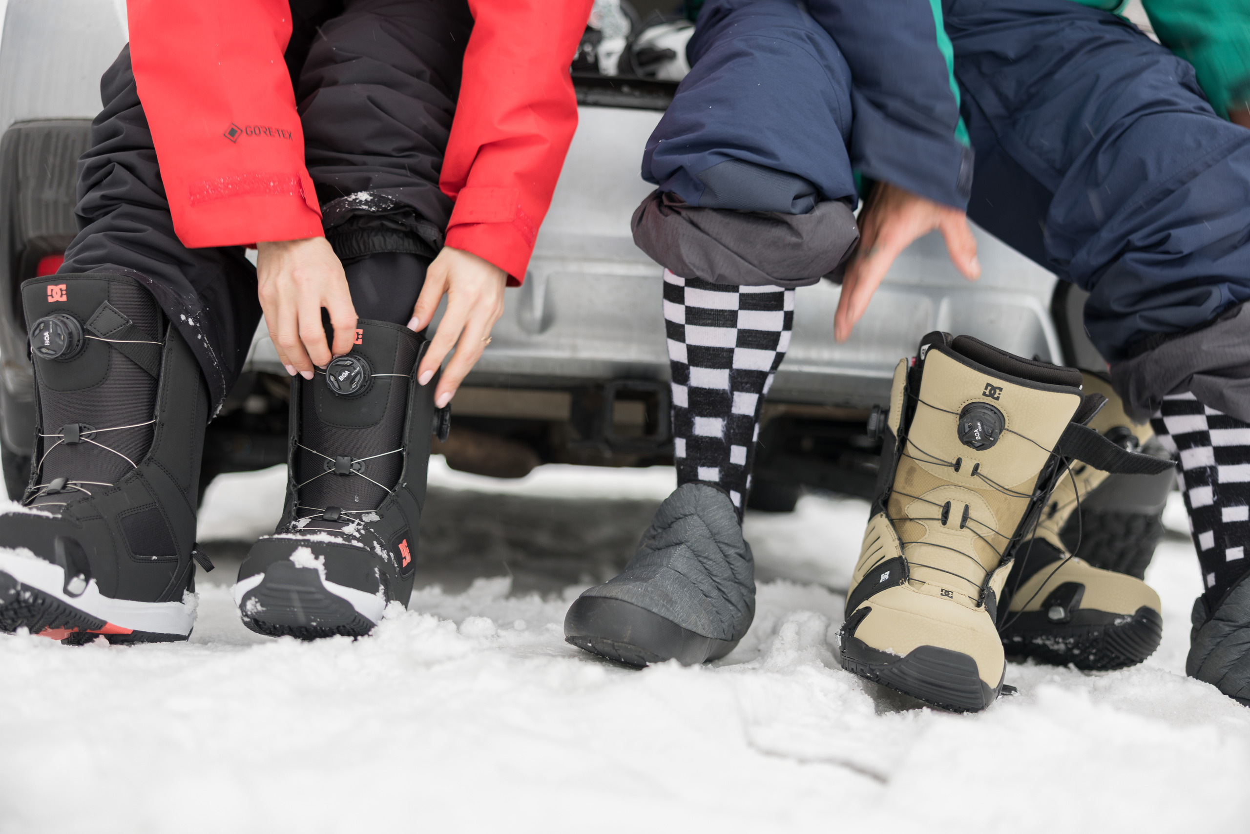 Two snowboarders sit on the back of their vehicle to put on snowboard boots with BOA dials