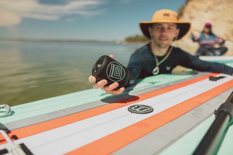 A paddle board sets a music speaker on top of the paddle board.