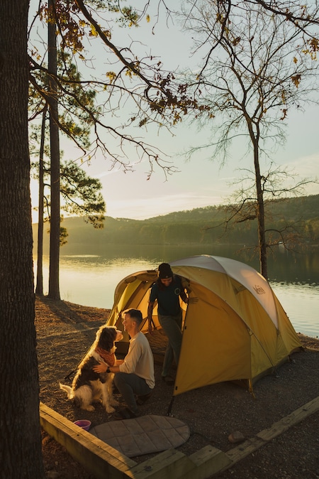 A man, woman and dog in front of a tent by water