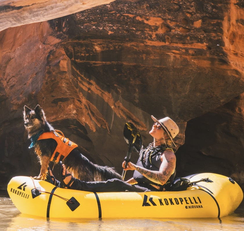 A person and their dog float through a body of water in a packraft.