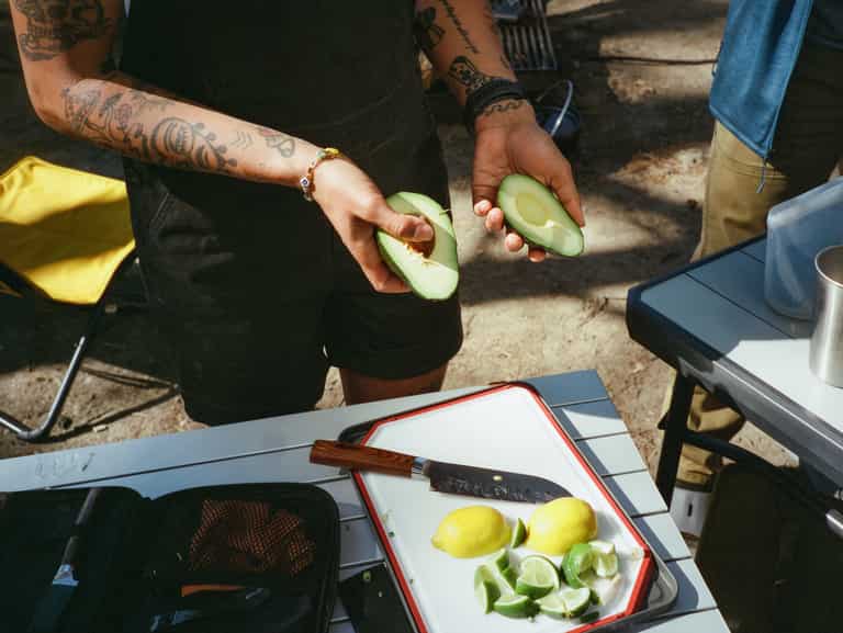 Picture of a person holding two halves of one avocado. A cutting board with lime wedges and a lemon is below their hands.