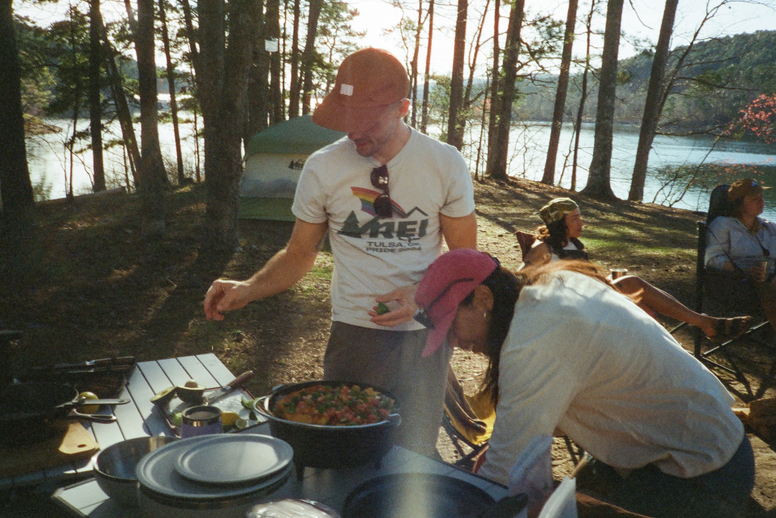 two people cook outdoors using a dutch oven at a waterside campsite