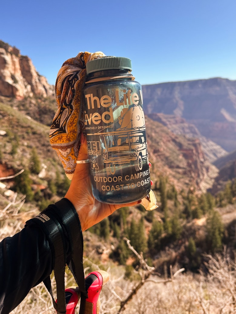 A person shows off their Nalgene water bottle while on a hike.