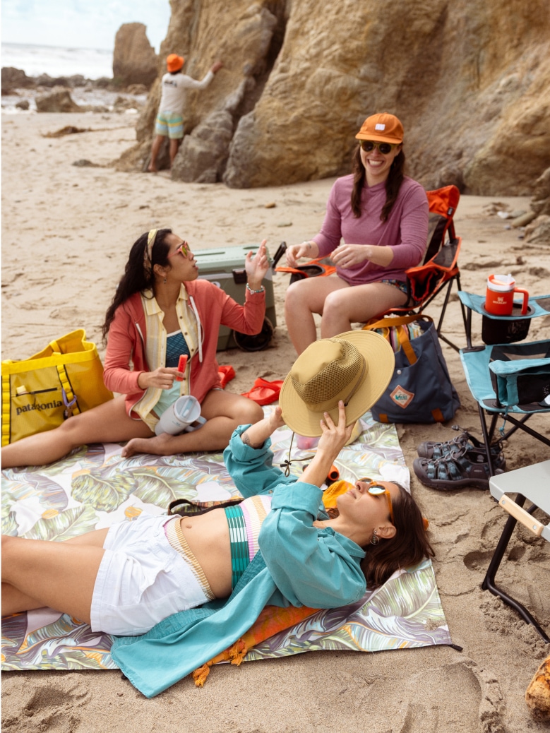 Three people laugh while relaxing at their setup on the beach. 