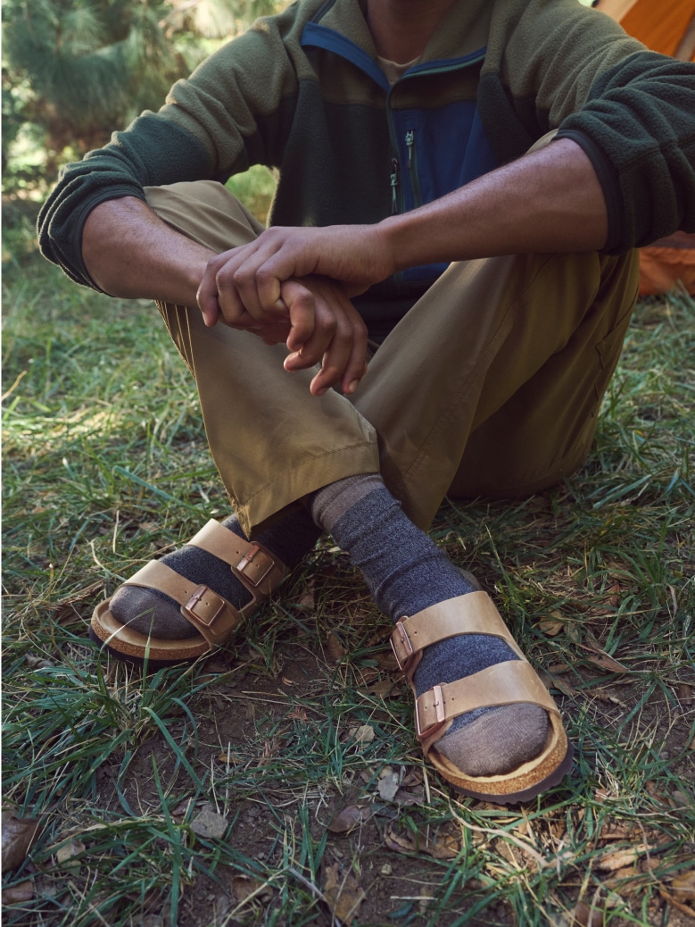 A person sits in the grass while wearing their Birkenstock sandals.