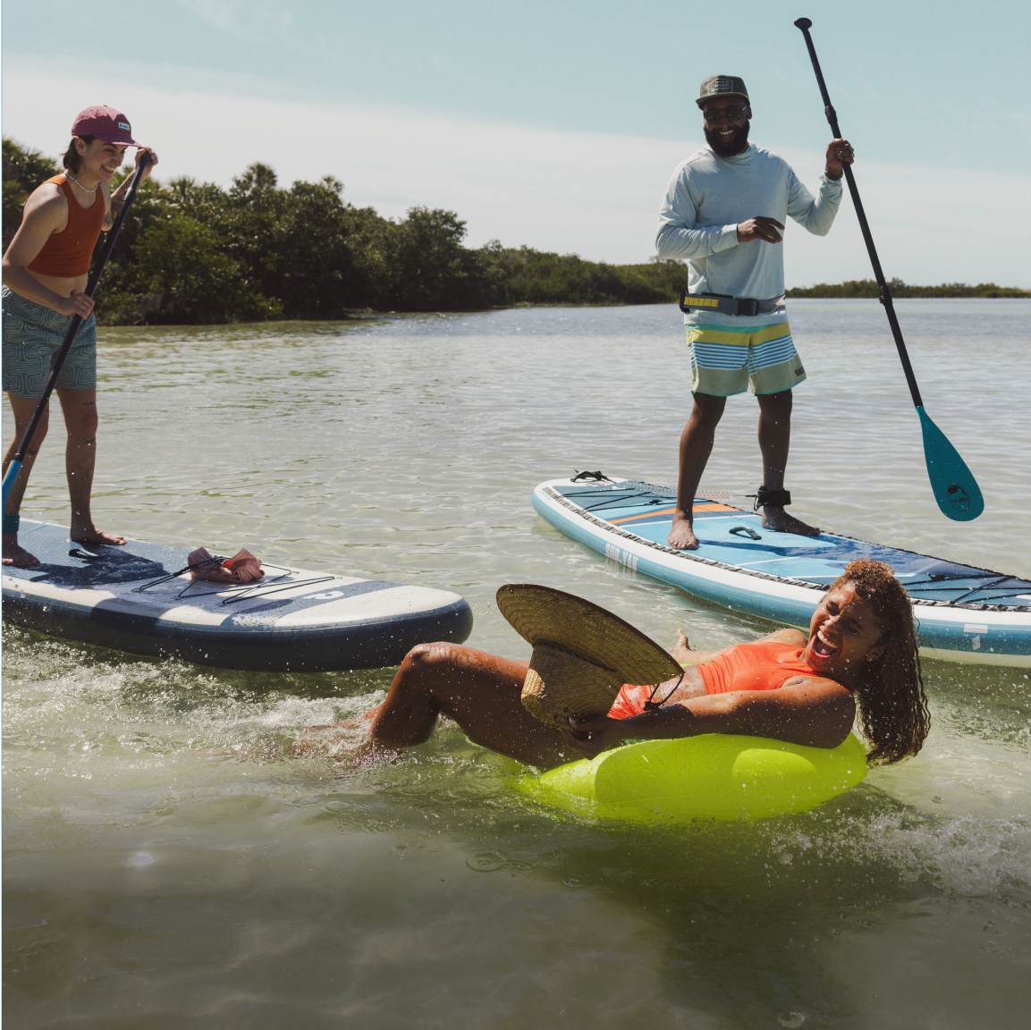 Two people on paddle boards splash another person while enjoying their day on the water.