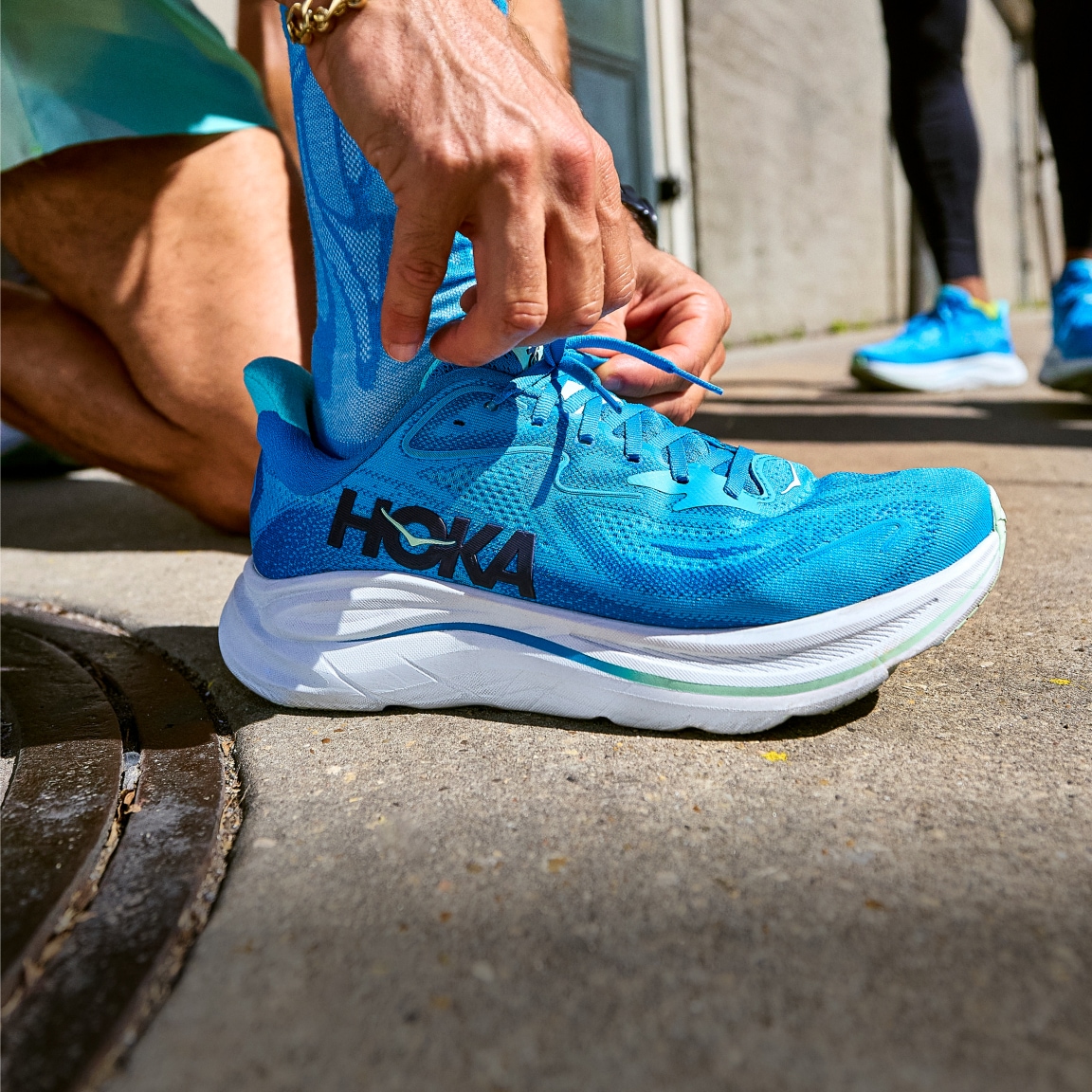 A person ties their HOKA shoe before a run.