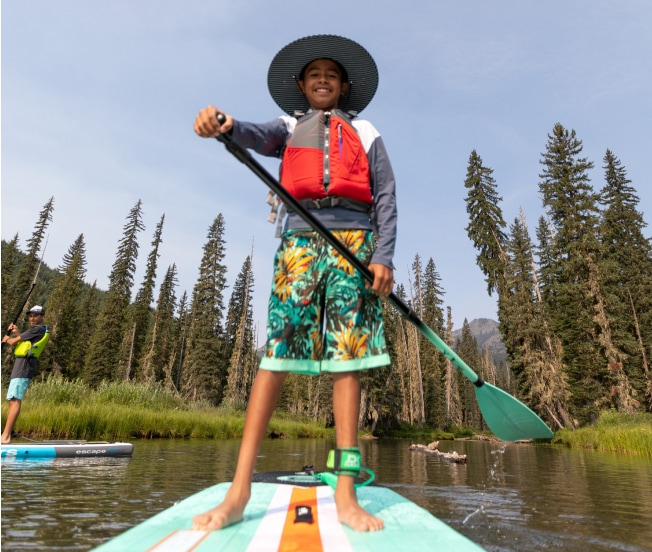 A person stands on a paddle board and smiles for the camera.