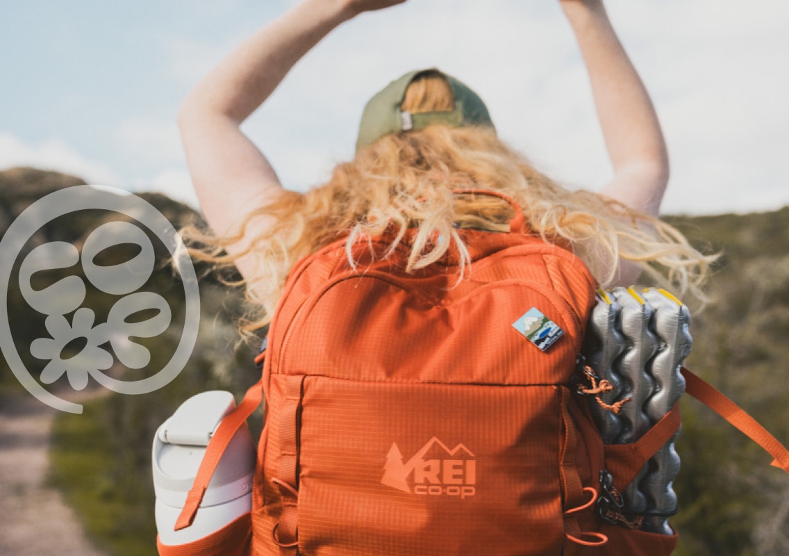 A person wearing an R E I Co-op backpack throws their arms up in the air.