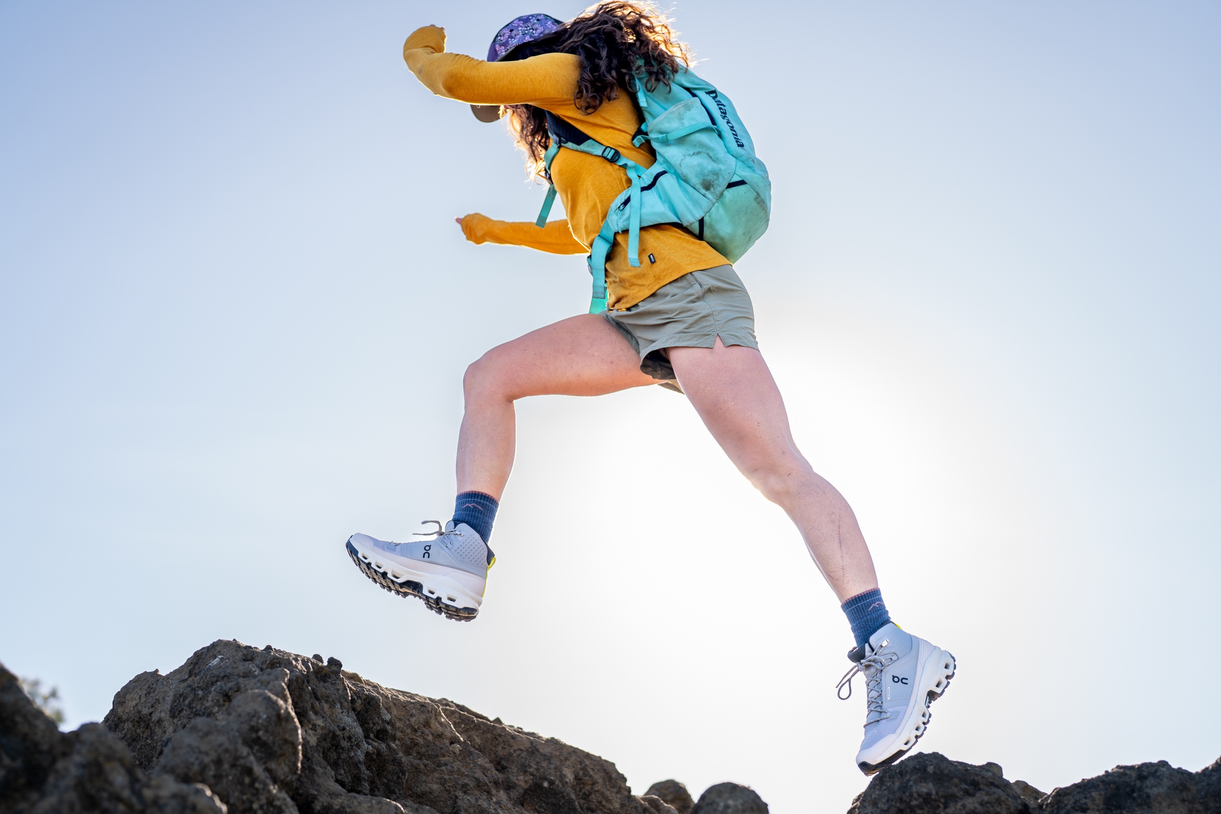 A person wearing a hiking pack and shorts jumps from one rock to another
