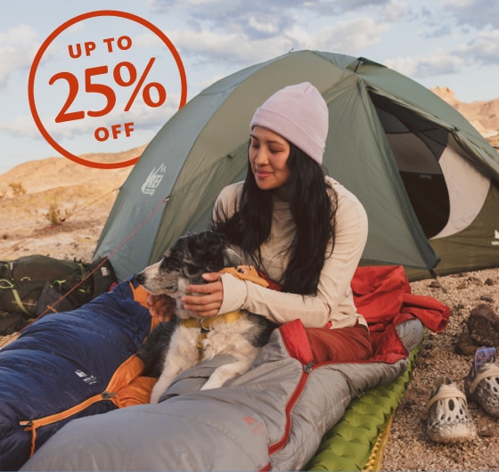 Up to 25% off. A person relaxes in a sleeping bag with their dog.