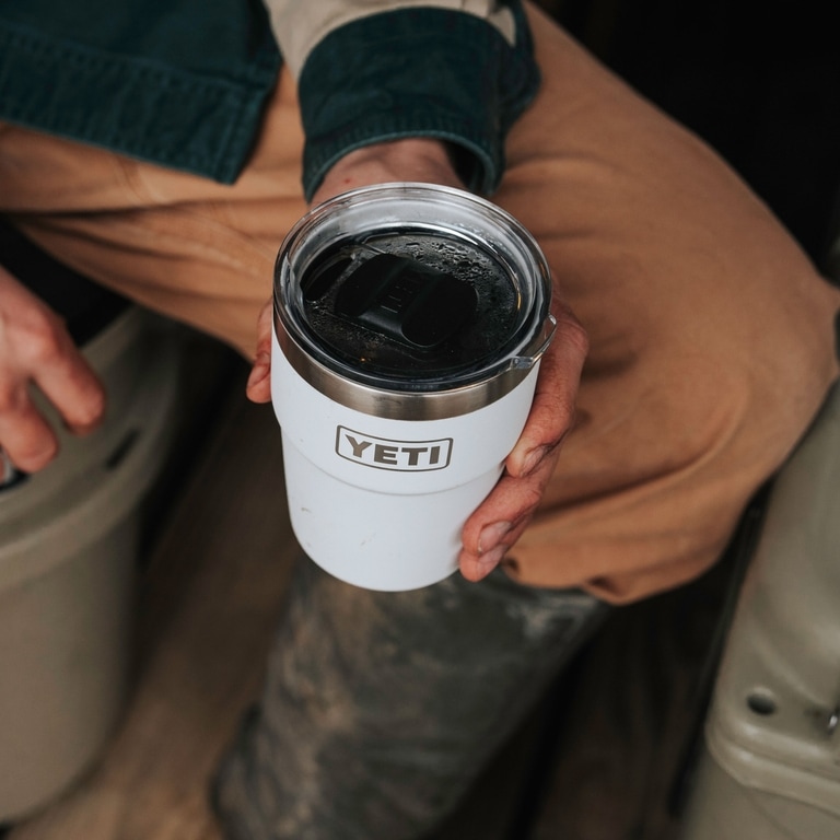A close-up picture of a hand holding a white YETI camp mug