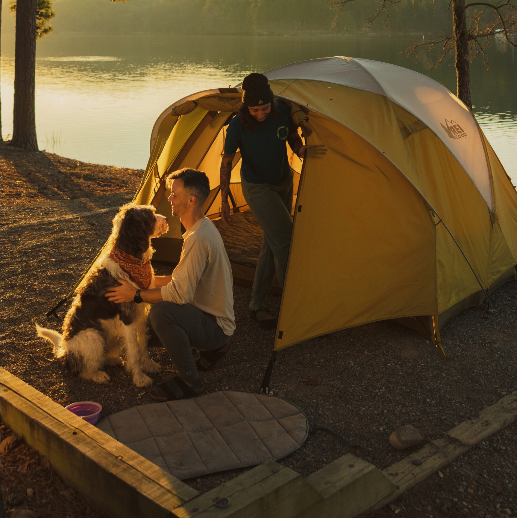 R E I Co-op, Zempire, & YETI. Two people enjoy time with a dog at their campsite.