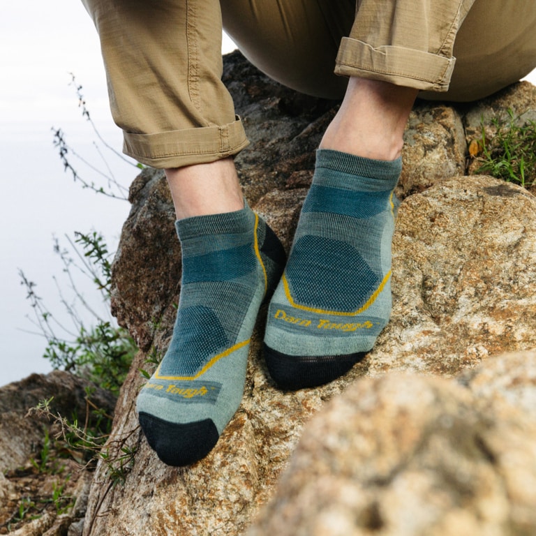 A person sits on a rock with their sock feet resting on the rock face.