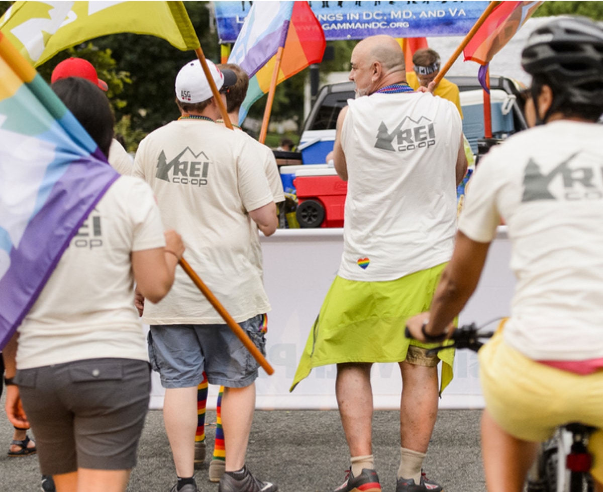A group of people in R E I Co-op shirts march with Pride flags.