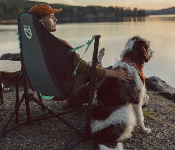 A person sits in their camp chair while watching the sunset with their dog.