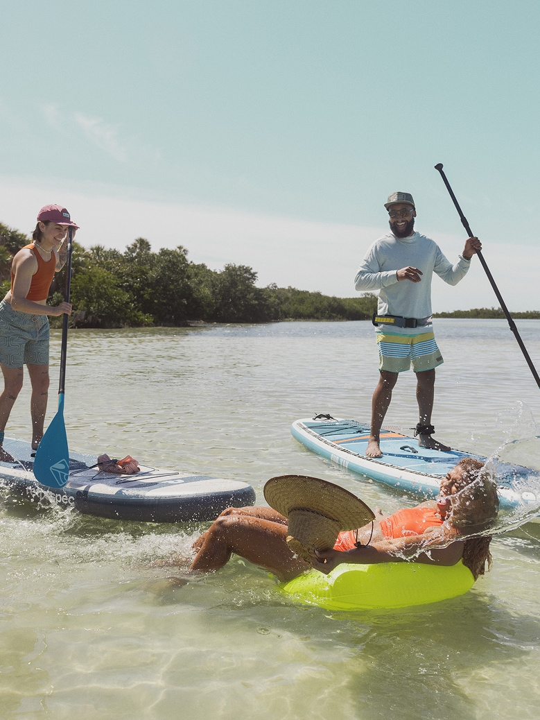 Two people on paddle boards splash another person while enjoying their day on the water.