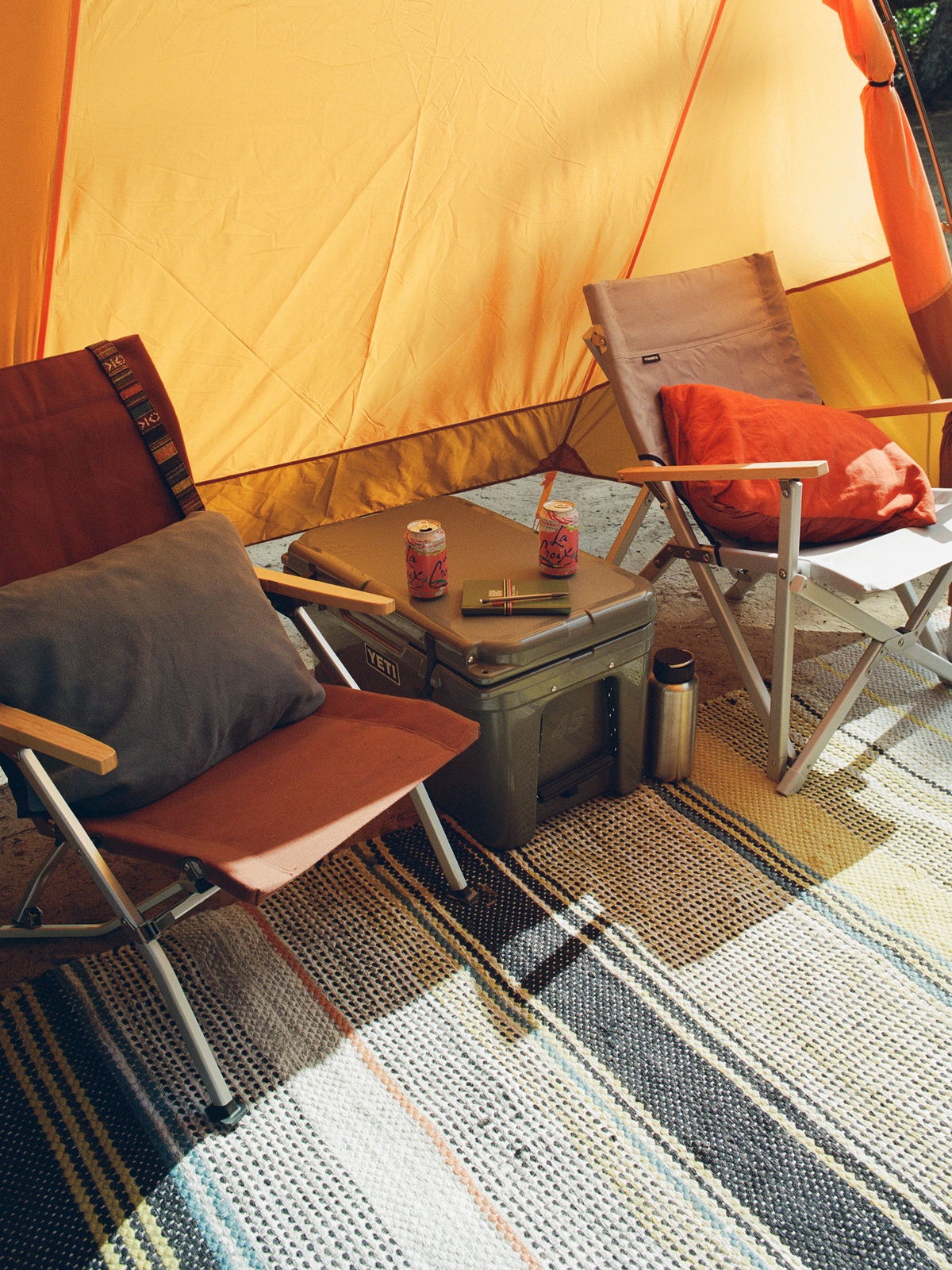 A campsite setup with two chairs, a cooler, and a blanket.