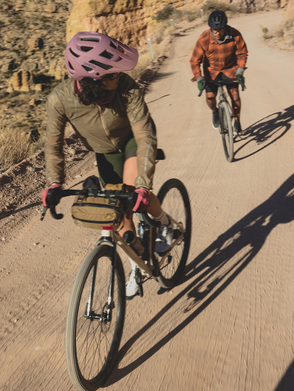 Two people bike down a desert trail.