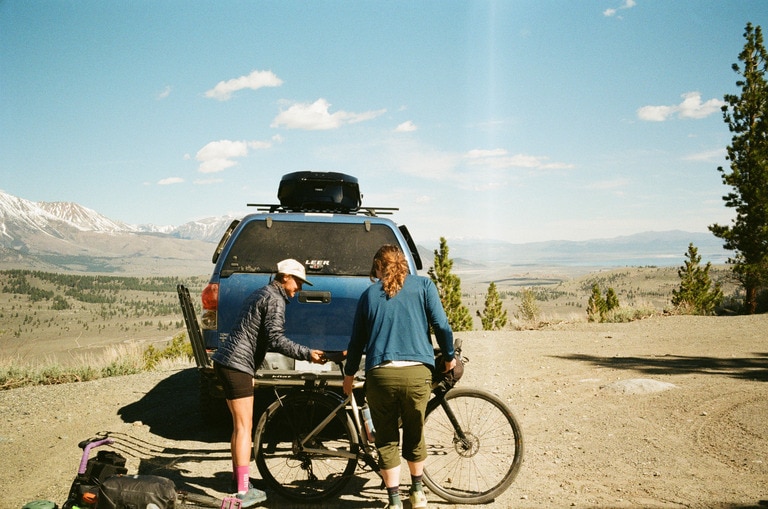 Two cyclists load a bike on a car bike rack.