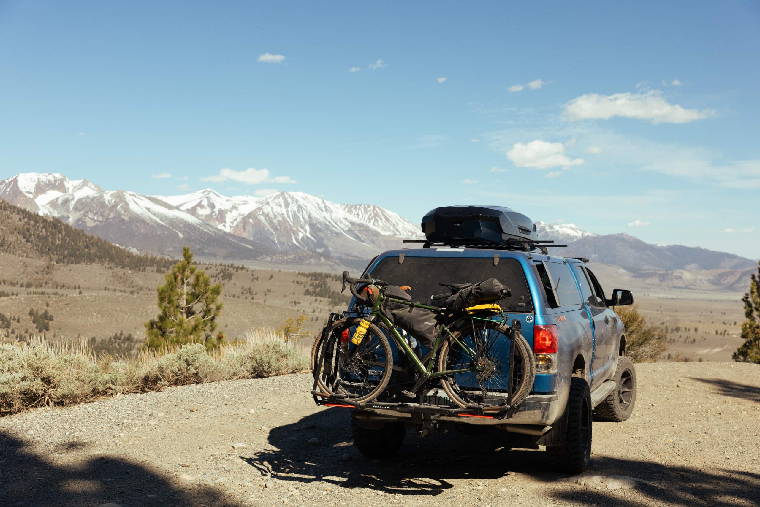 A car hauls a roof cargo box and two bikes on the bike rack