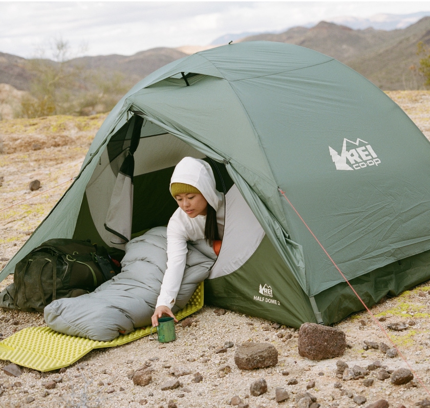 A camper sits in their Half Dome tent and grabs their mug.