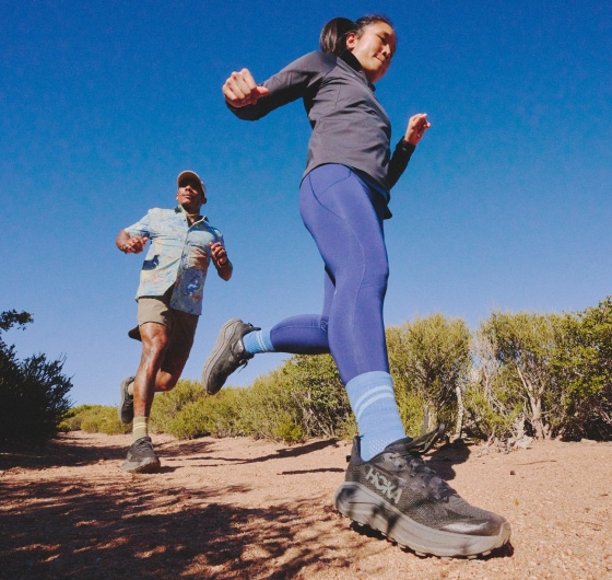 Two people run through a rugged trail on a sunny day.