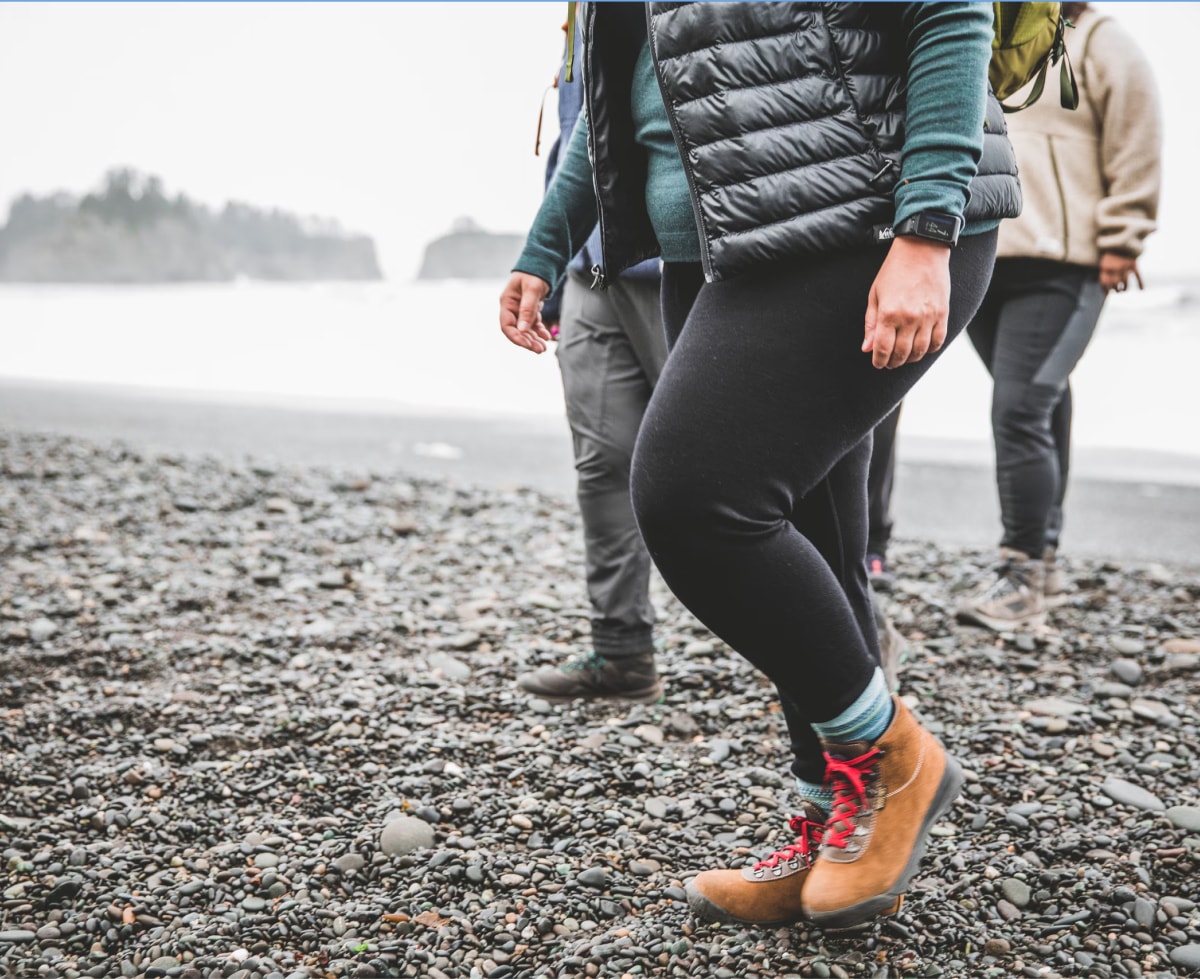 Three people walk along a rocky shoreline on a cold day.