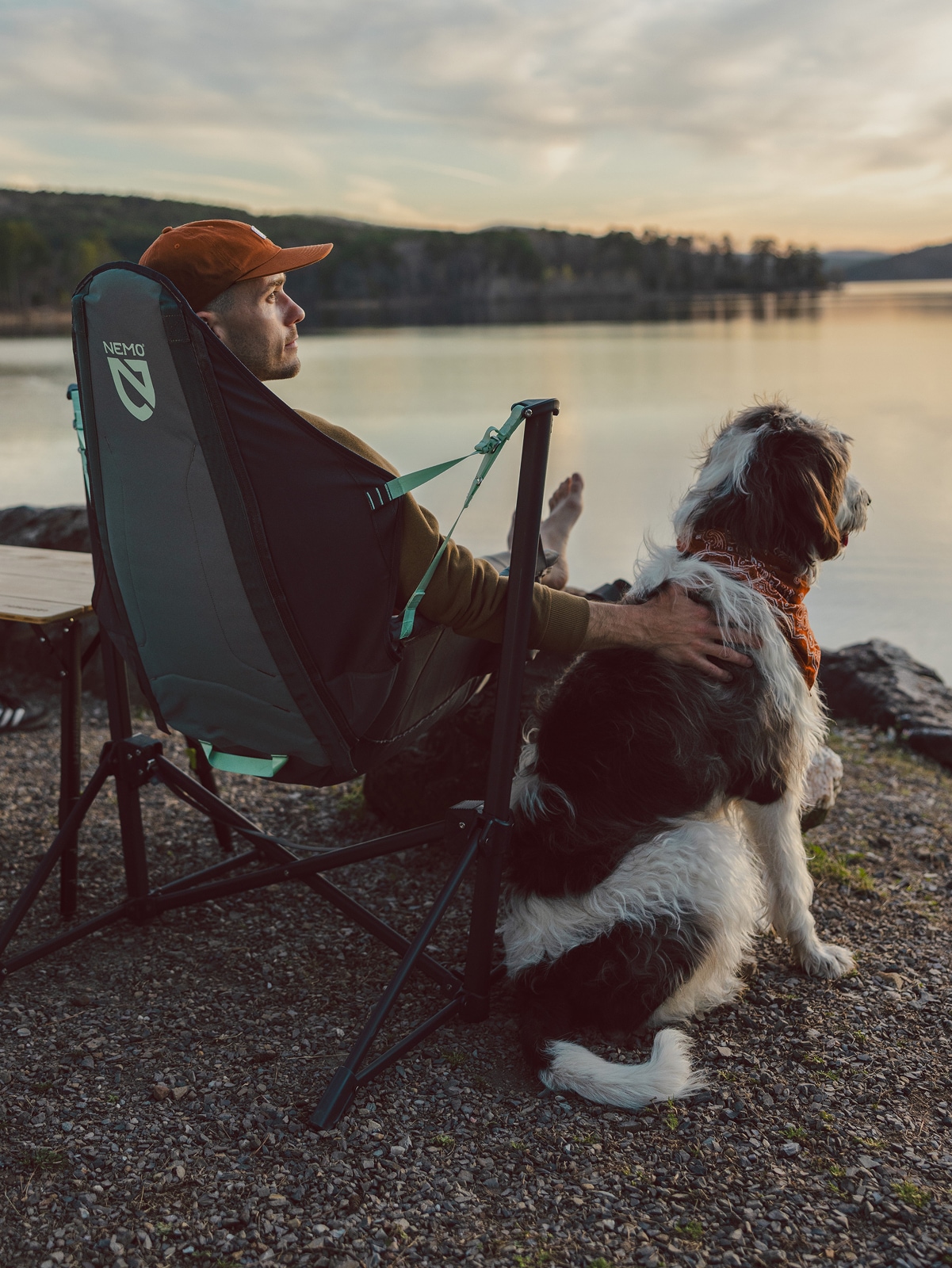 A person sits in their camp chair while watching the sunset with their dog.