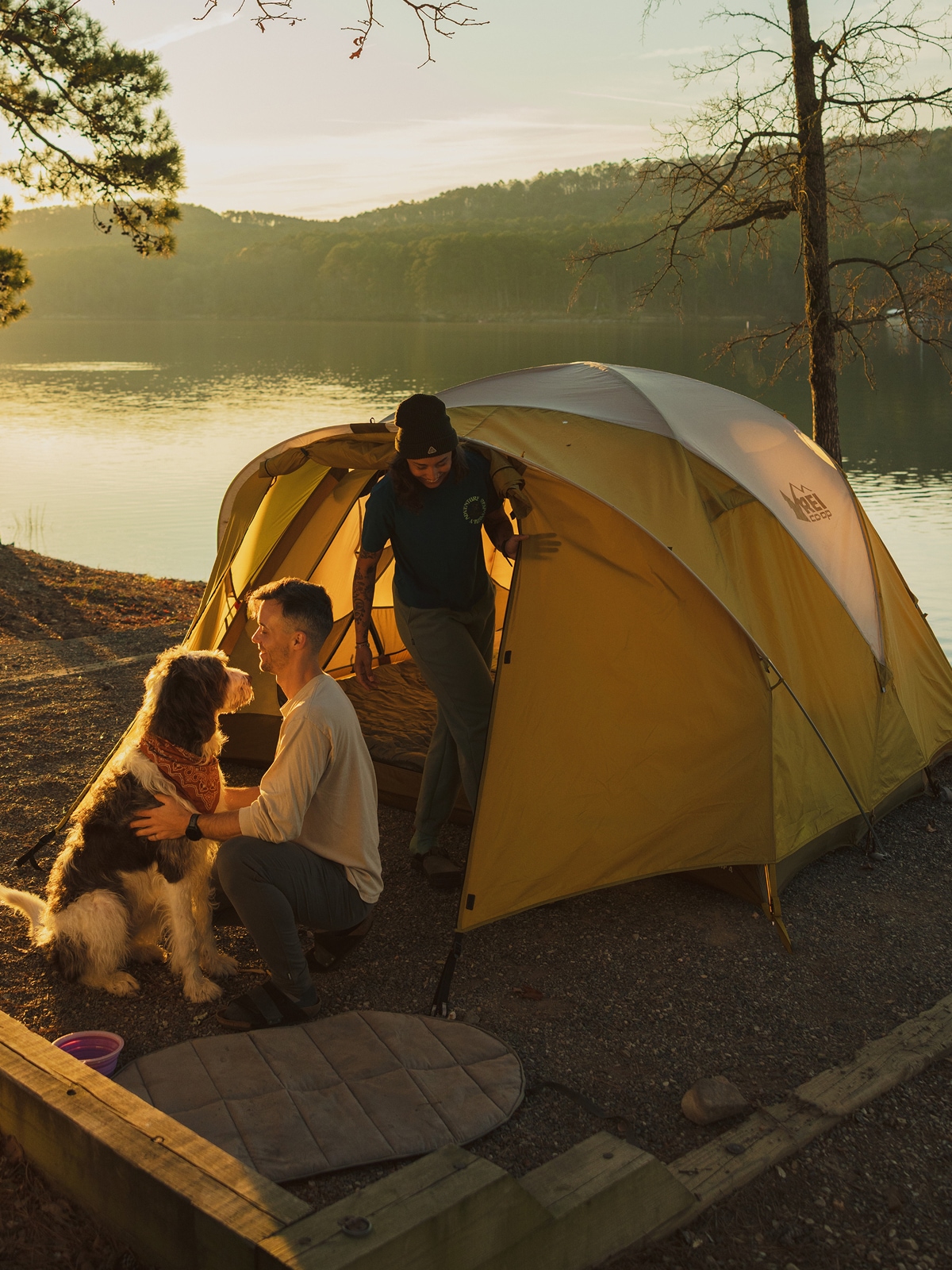 Two people and a dog relax outside their tent.
