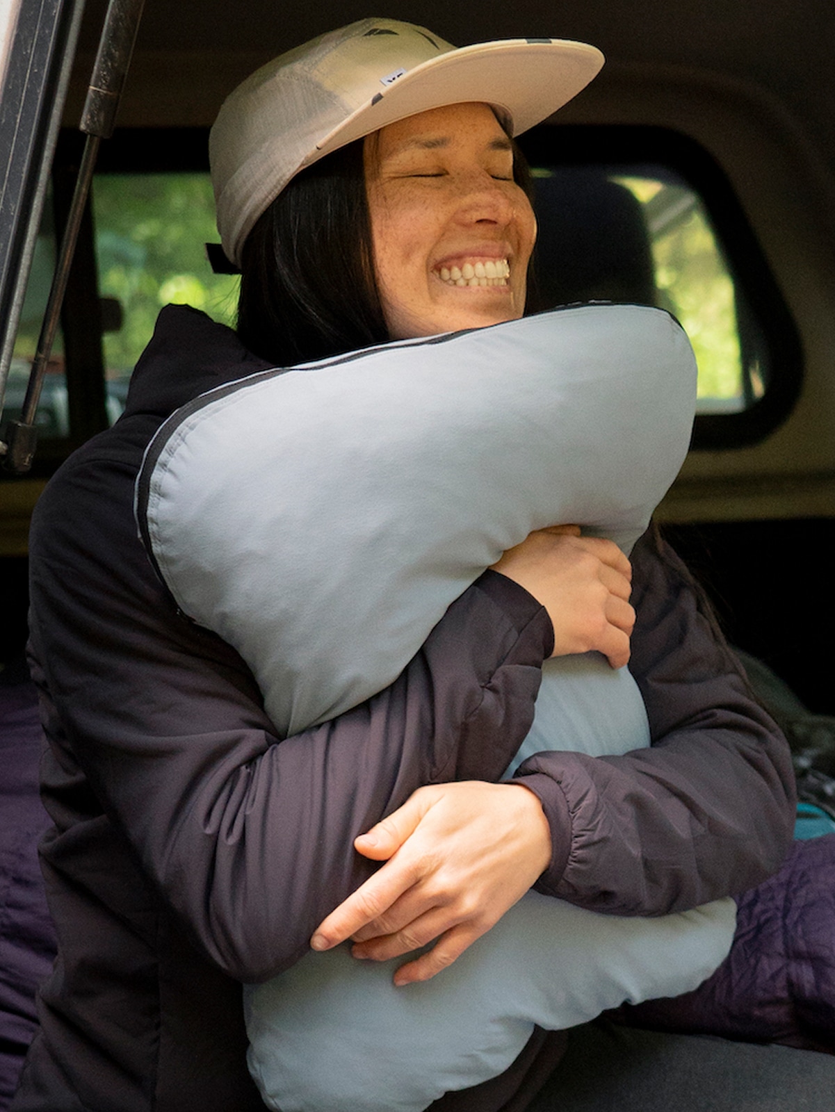 A person hugs their pillow & smiles for the camera.