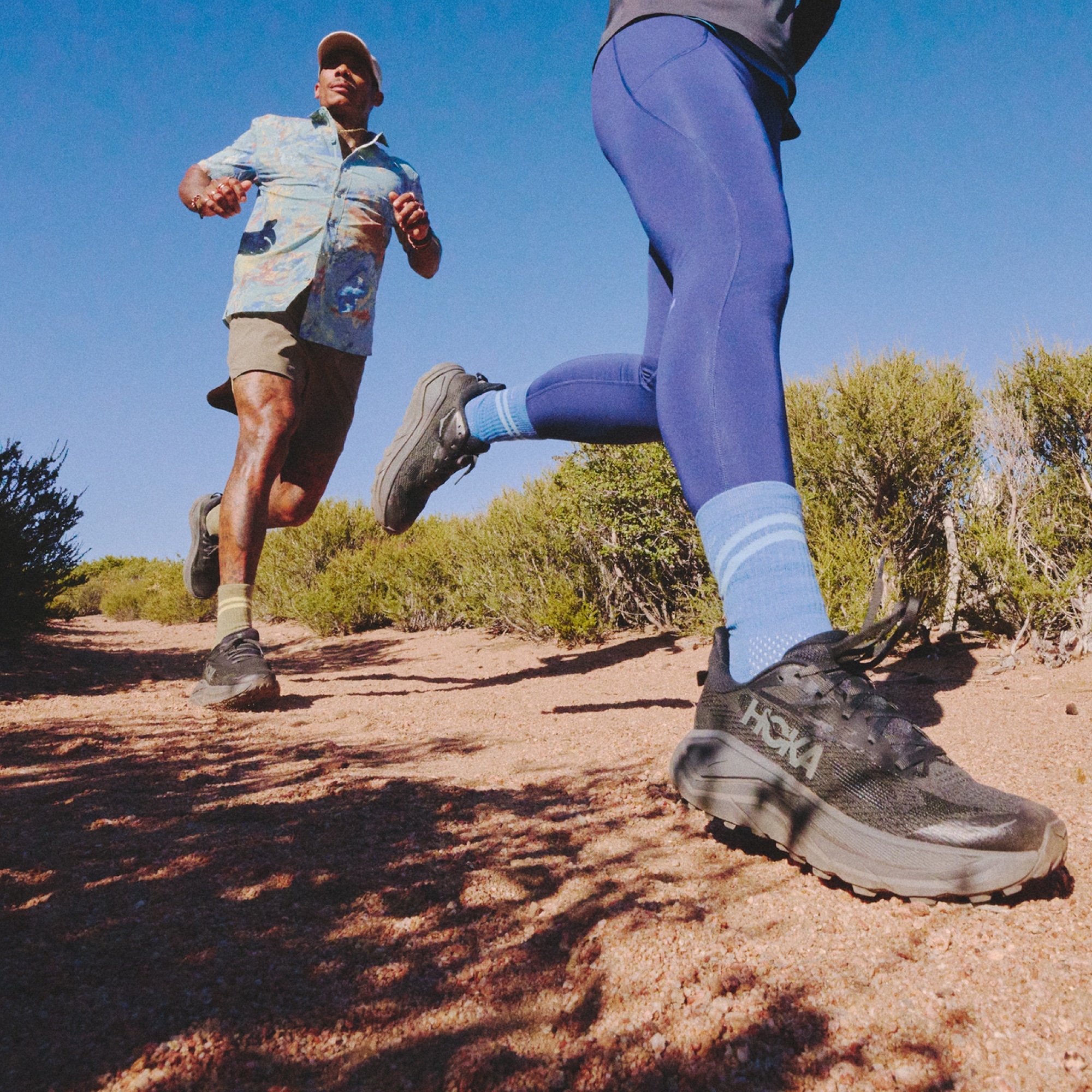 Two people jog down a rocky trail on a sunny day.