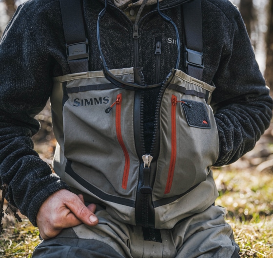 A person sits down in their Simms fishing gear.