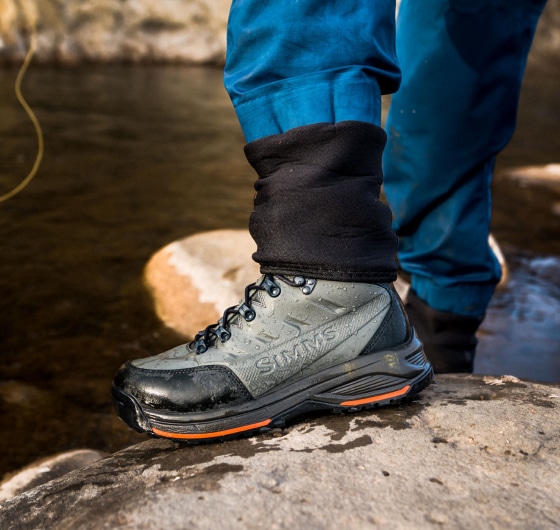 A person stands on a rock in their Simms wading boots.