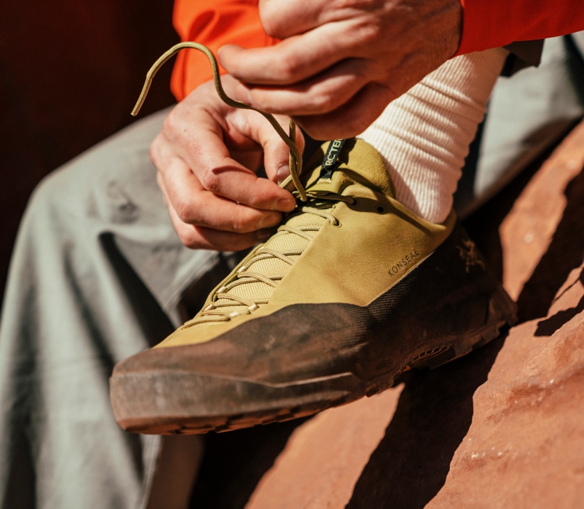 A person sitting down while tying their Arc'Teryx Konseal shoe.
