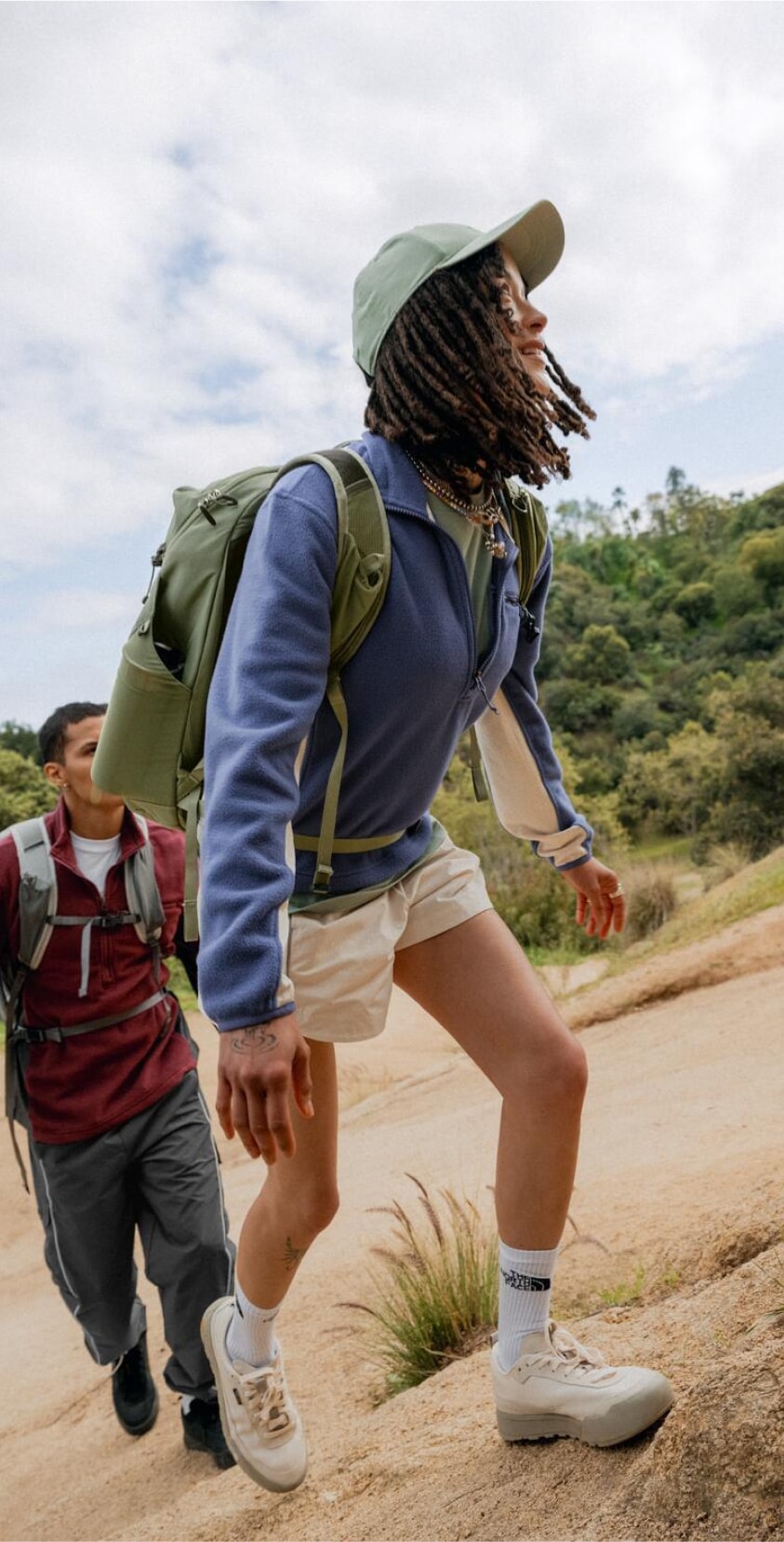 Two people hike up a steep path on a partly cloudy day.