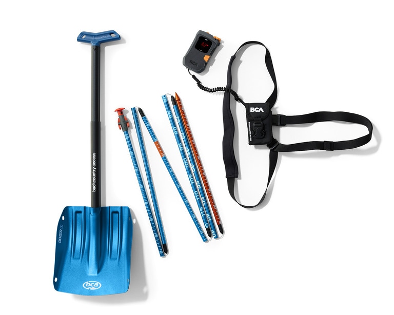 A photo laydown of snow shovel, probe and avalanche transceiver
