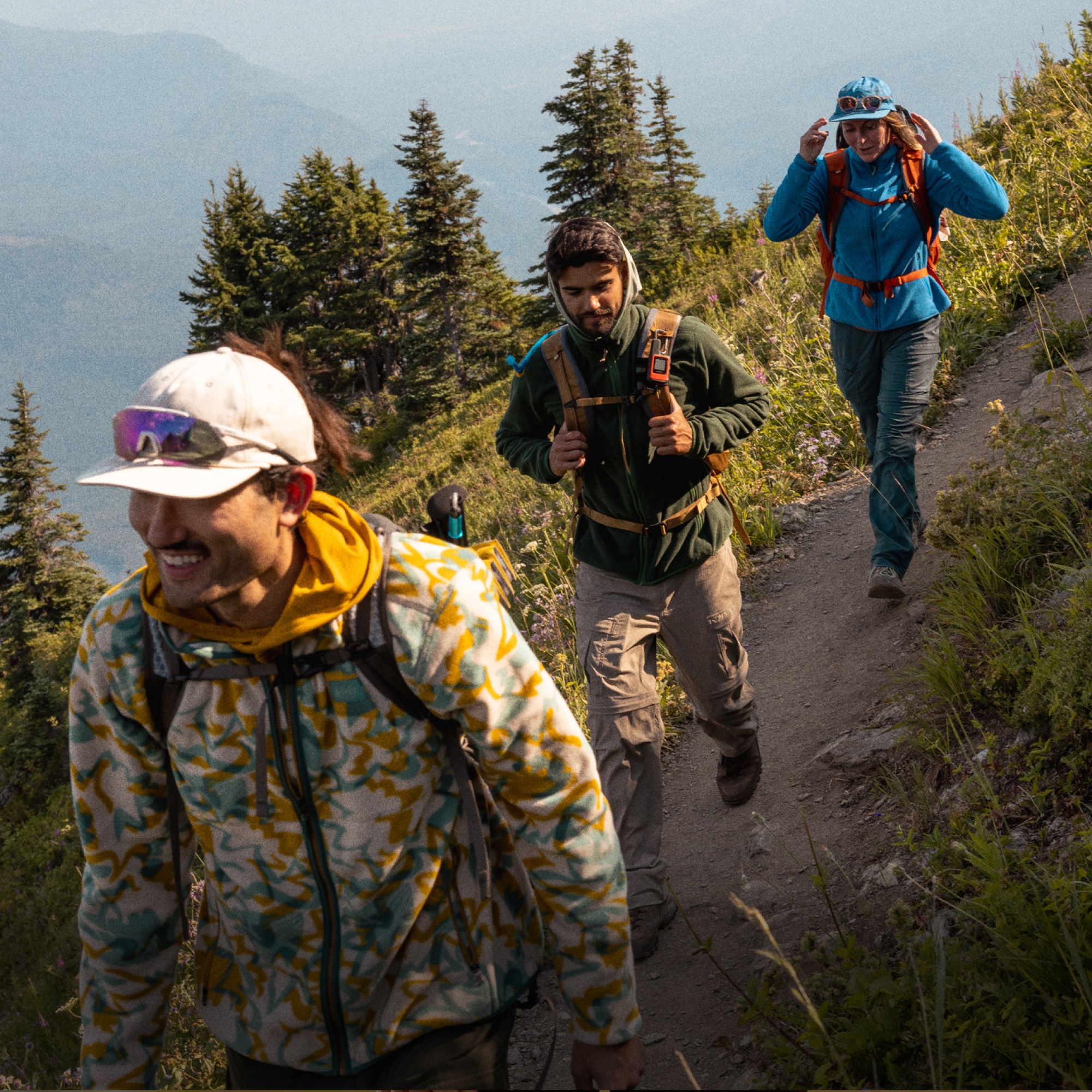 Three people hike down a rocky trail in fleece clothing.