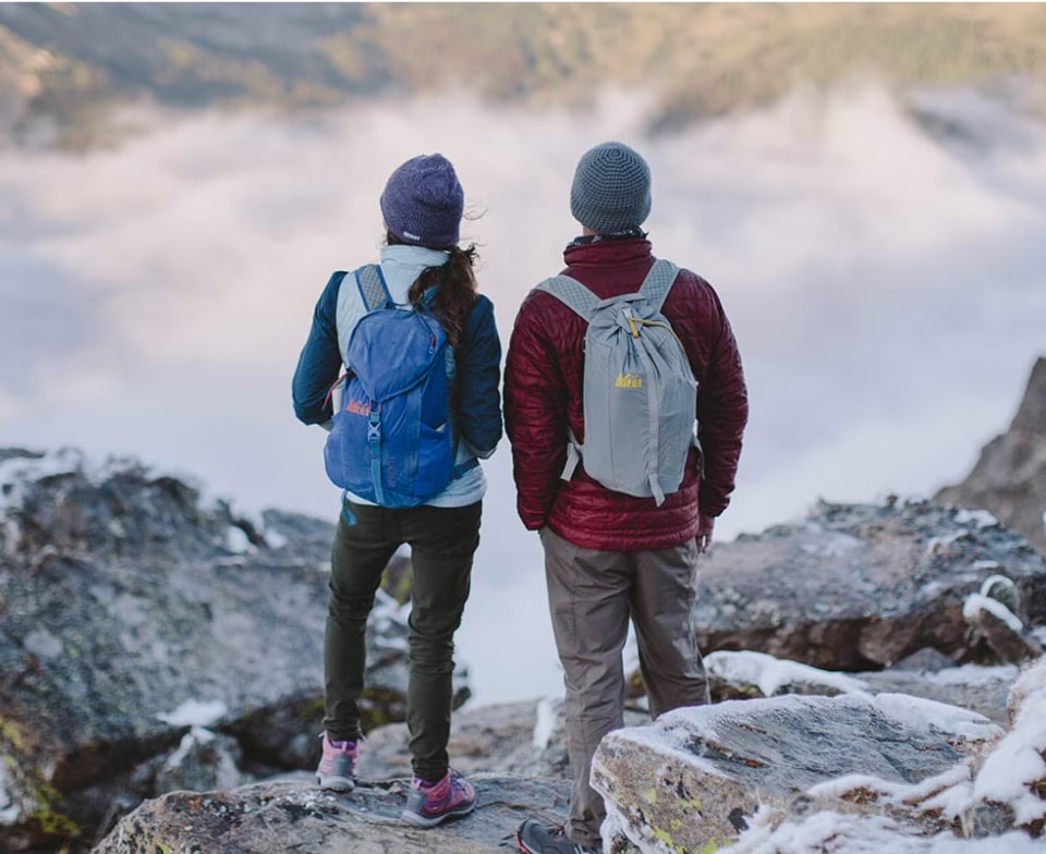 Two people stand on a rock and look out over the mountains on a cold day.