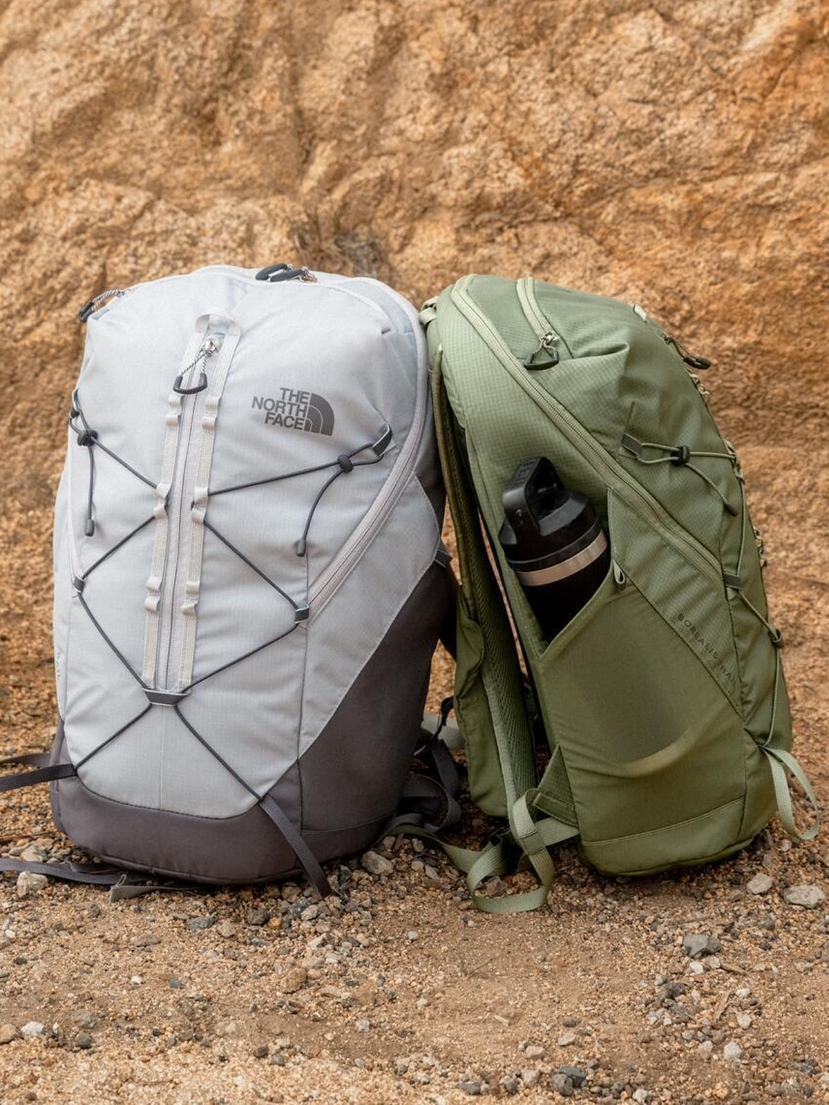 Two North Face backpacks leaned up against each other on a rocky path.
