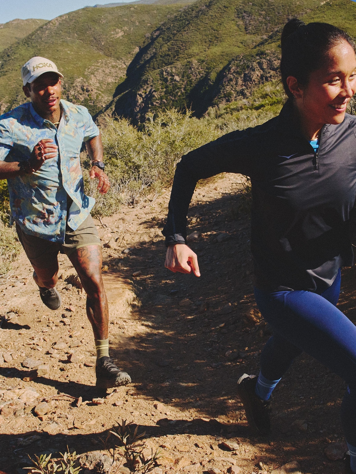 Two people run on a rocky trail on a sunny day.