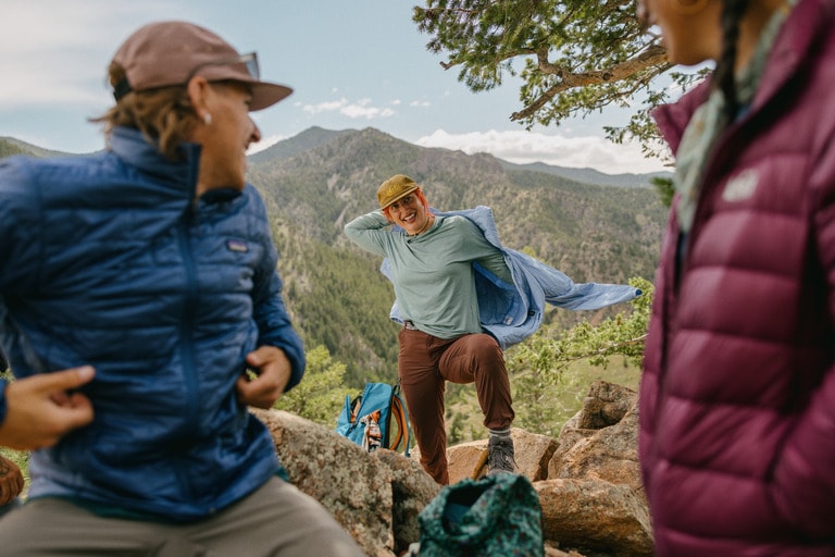 Three people hiking take a break to throw on extra layers