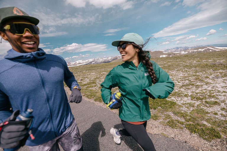 Two smiling runners; the one on the left wears a lightweight blue fleece jacket with a textured pattern
