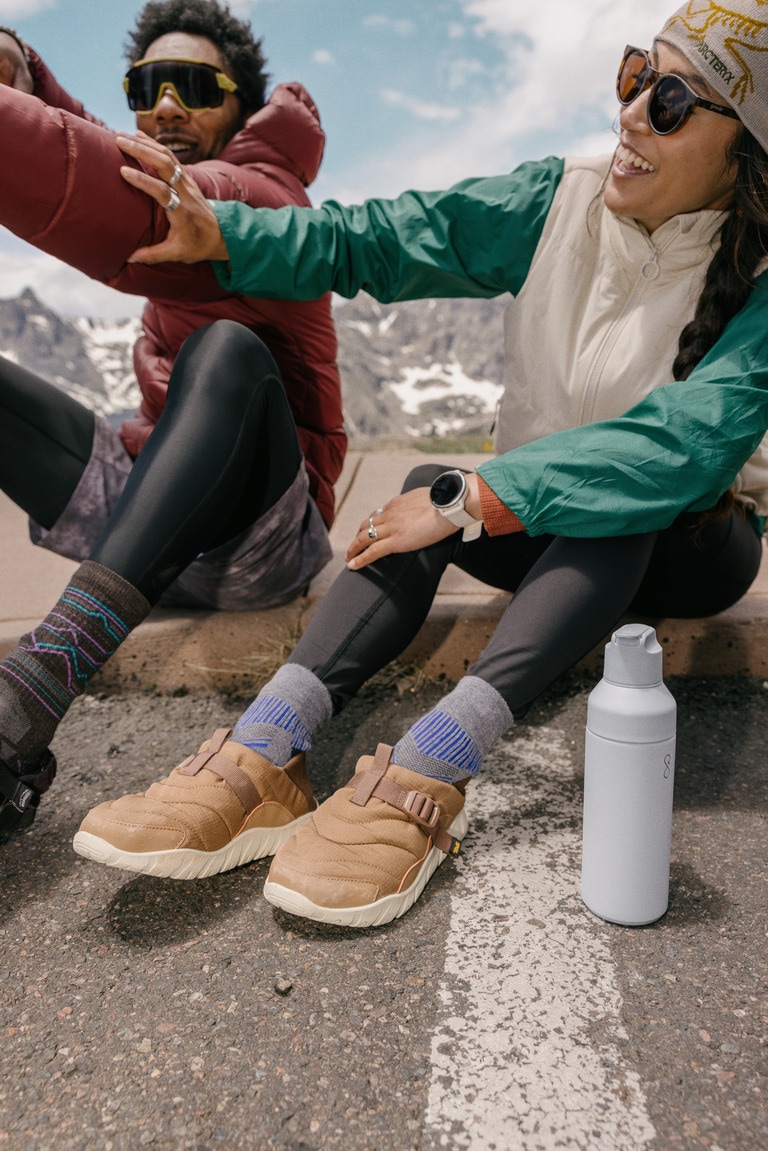 Two people sitting on a road outside; one wears the Garmin vivoactive 6 fitness smartwatch.