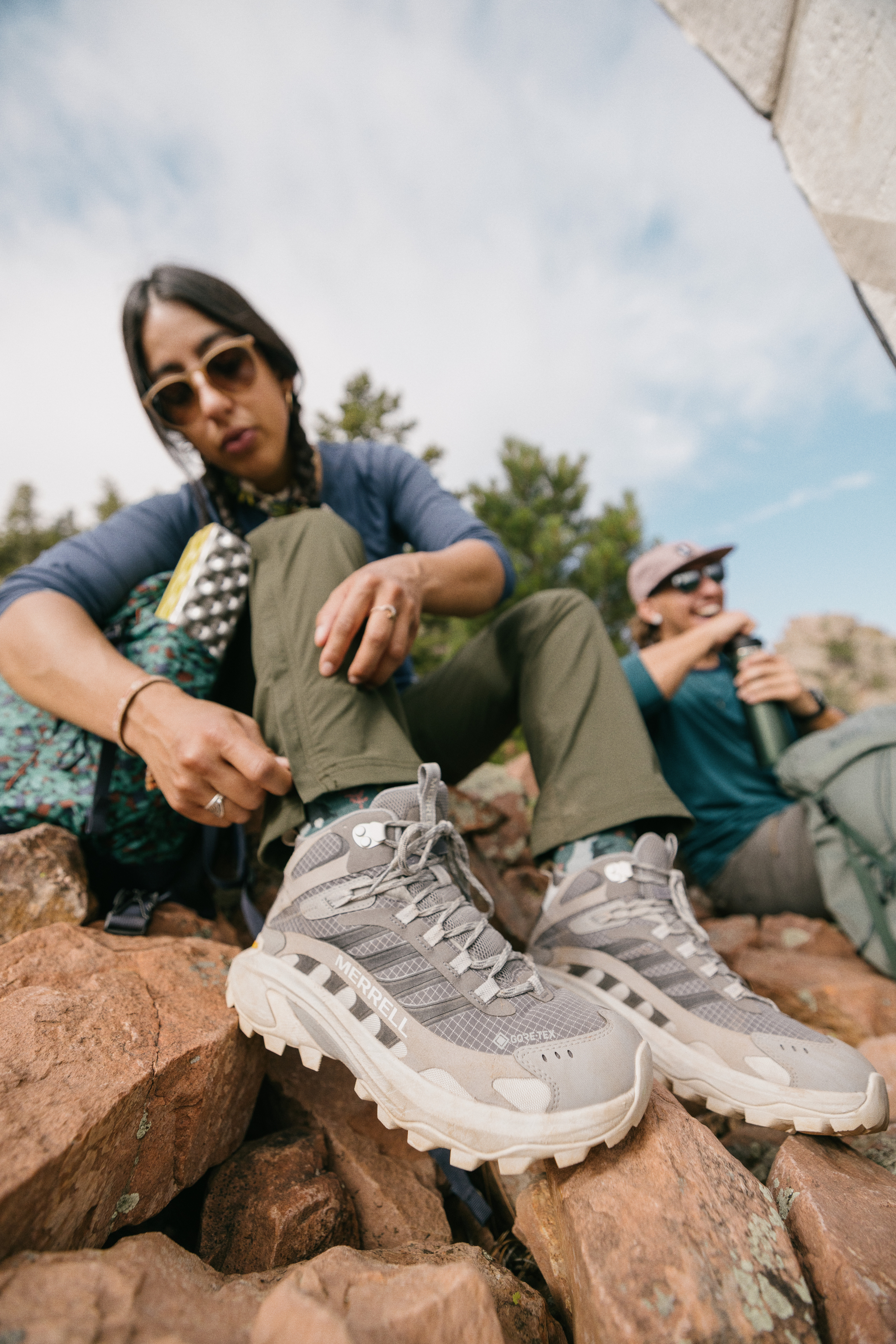 A person sitting on a rock adjusts their hiking pants around their Merrell hiking boots