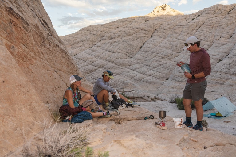 Three people preparing food during a fastpacking trip in a western mountain range.