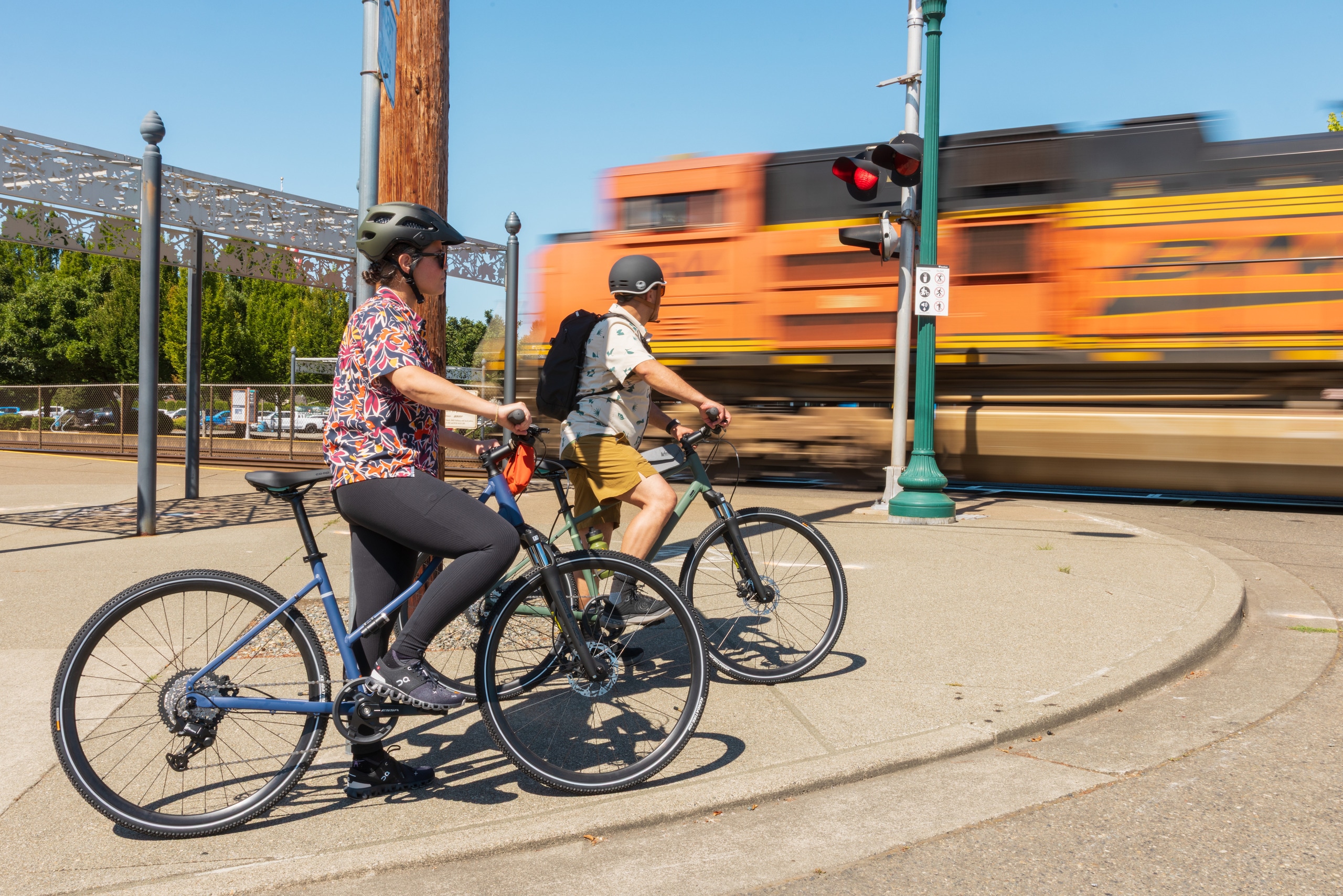 Two cyclists stop to let a train pass by while biking in the city.