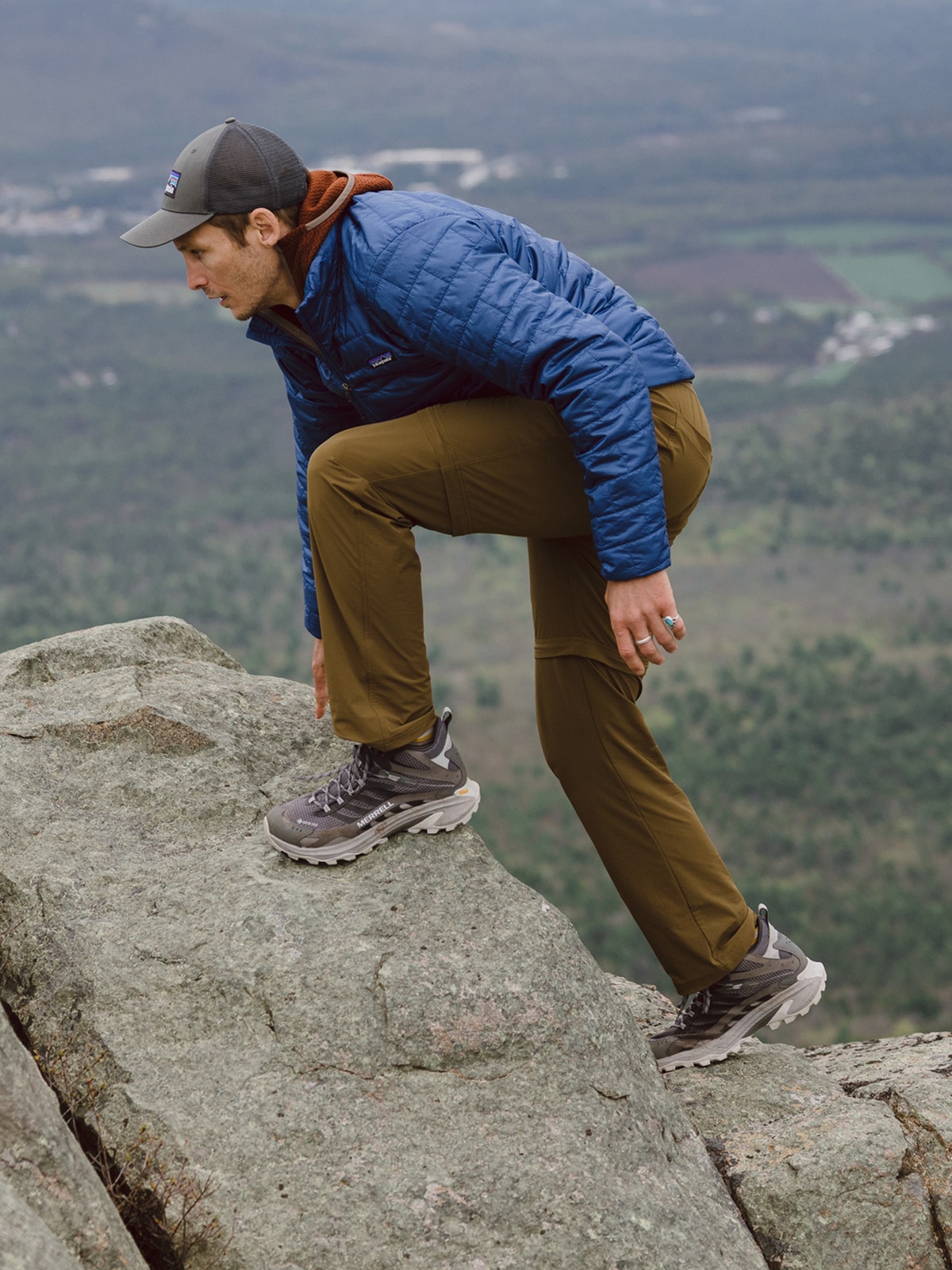 A person makes their way up large rocks while on a hike.